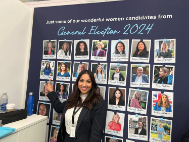 Shivani Raja MP stood next to a photograph of herself on a board of new female Conservative MP's